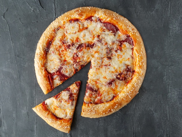 Italian pepperoni pizza. With pepperoni sausage, tomato sauce, Mozzarella cheese, Sulguni and Parmesan. A piece is cut off from pizza. View from above. On a gray concrete background. Isolated.