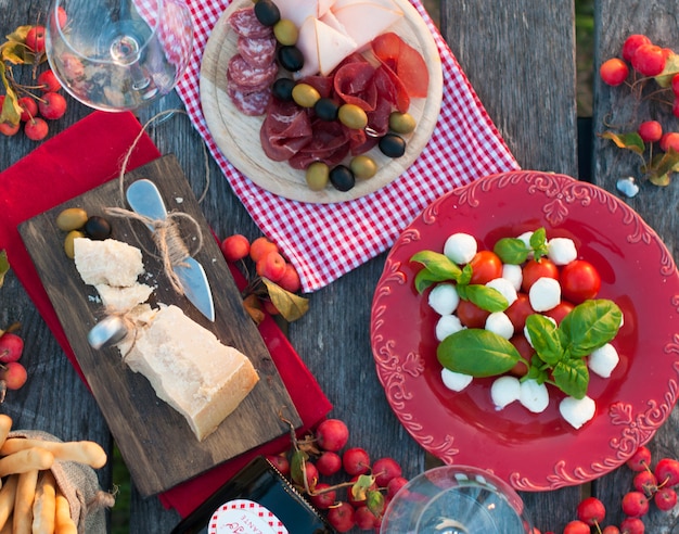 Italian picnic with red wine, Parmesan, ham, caprese salad and olives. Lunch in the open air and wooden table. Traditional snacks. Copy space