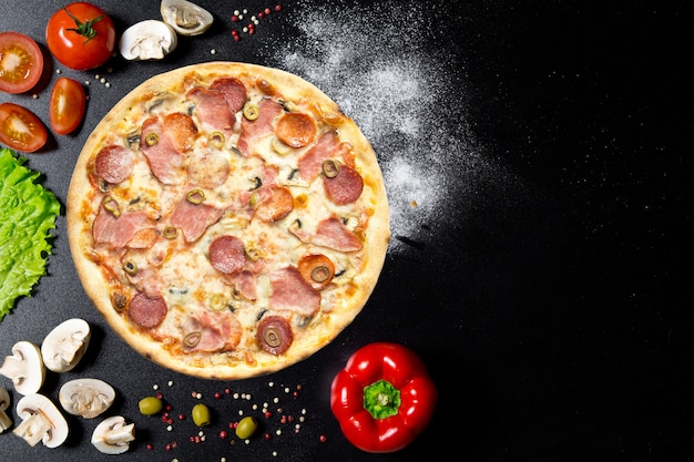 Italian pizza and ingredients. Mushrooms, tomatoes, pepper, salt, herbs and alive on a black concrete table. Top view