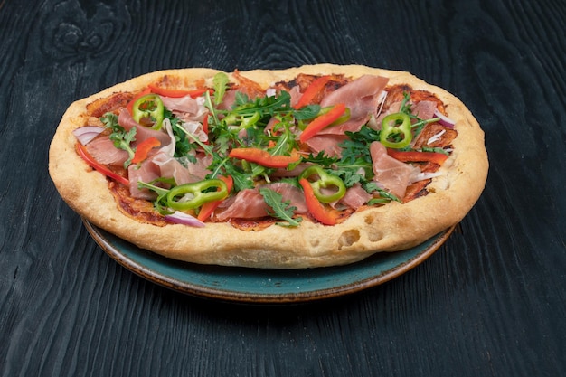 Italian pizza on plate with jamon slices pepper and fresh arugula leaves on top