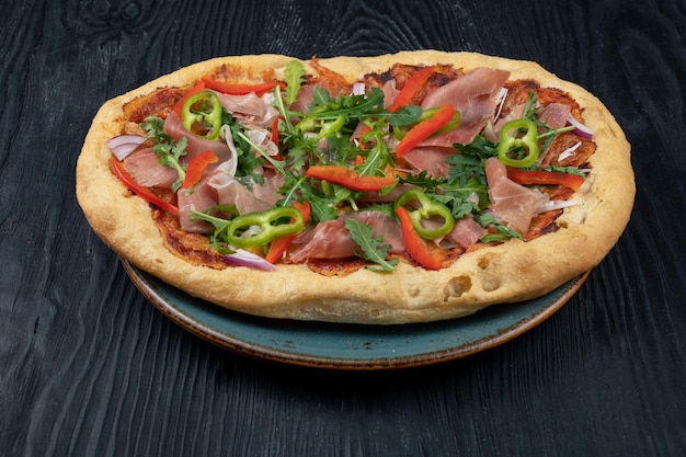 Italian pizza on plate with jamon slices pepper and fresh arugula leaves on top