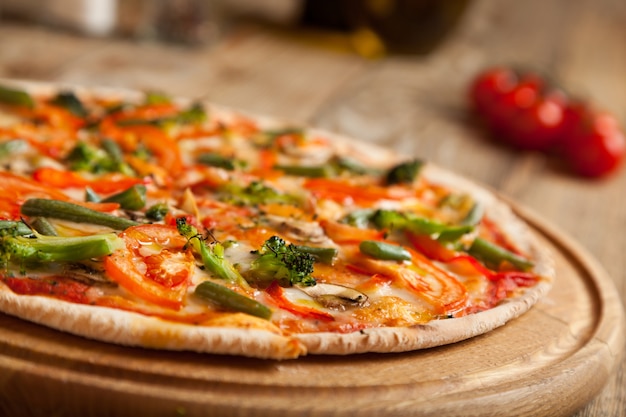 Italian pizza "Vegetarian" on wooden table. On top of the pizza are baked sliced tomatoes, and asparagus broccoli. Nearby are containers with spices and olive oil. Near them are cherry tomatoes.