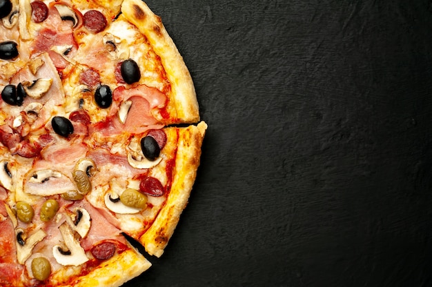 Pizza italiana con pancetta, funghi, olive, pomodori su uno sfondo nero di cemento con copia spazio per il testo