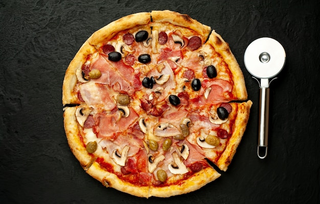 Italian pizza with bacon, mushrooms, olives, tomatoes on a black concrete background