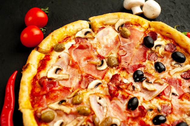 Italian pizza with bacon, mushrooms, olives, tomatoes on a black concrete background