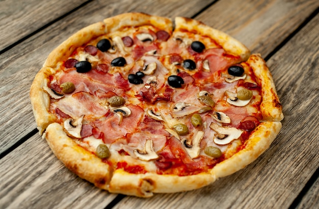 italian pizza with bacon, mushrooms, olives, tomatoes on a wood background with copy space for your text