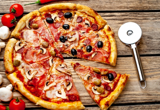 italian pizza with bacon, mushrooms, olives, tomatoes on a wood background