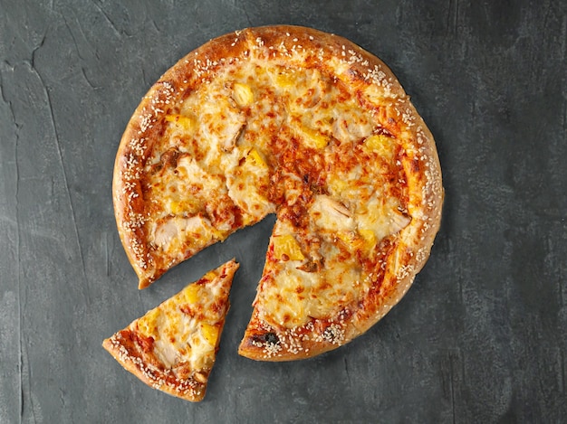 Italian pizza. With chicken, pineapple, tomato sauce, mozzarella cheese and sulguni cheese. Wide side. A piece is cut off from pizza. View from above. On a gray concrete background. Isolated.