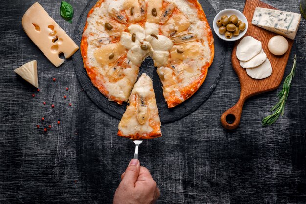 Pizza italiana con diversi tipi di formaggio su una pietra e una lavagna nera graffiata.