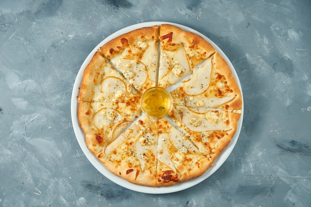 Italian pizza with pear and gorgonzola cheese on a white plate. Concrete surface. Top view