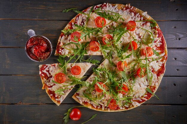 Italian pizza with tomatoes, cheese and herbs on vintage wooden table. Top view