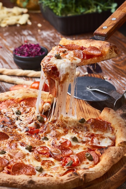 Italian pizza on a wooden table. a piece of hot pizza with\
cheese stretching.