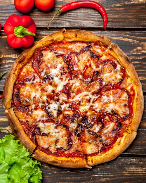 Italian pizza on a wooden table with ingredients, tomatoes, peppers, onions