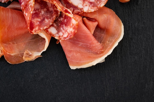 Italian prosciutto crudo or spanish jamon and sausages. Raw ham on stone cutting board