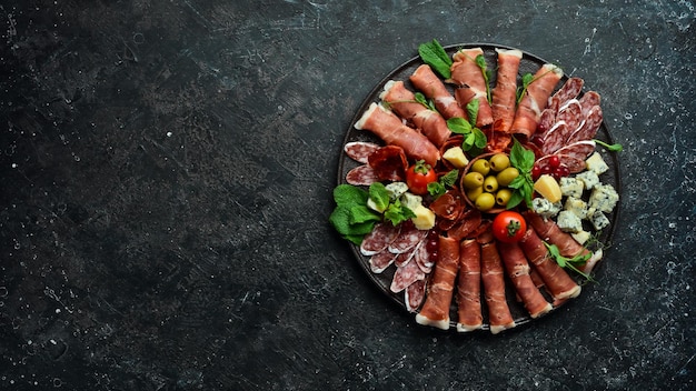 Italian prosciutto dried pork parmesan cheese olives and snacks on a plate Top view On a gray stone background