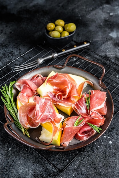 Italian prosciutto parma with melon and fresh rosemary Black background Top view