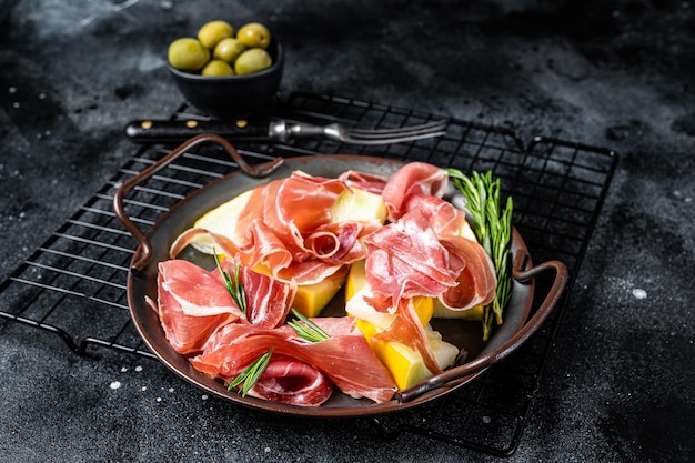 Italian prosciutto parma with melon and fresh rosemary Black background Top view