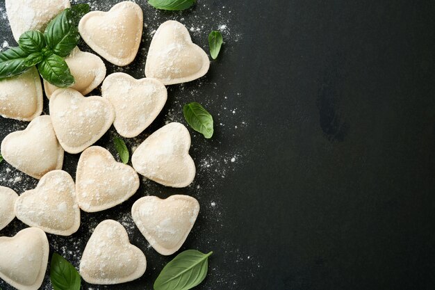 イタリアのラヴィオリパスタはハートの形で濃い背景の粉とバジルで作られた美味しい生ラビオリです