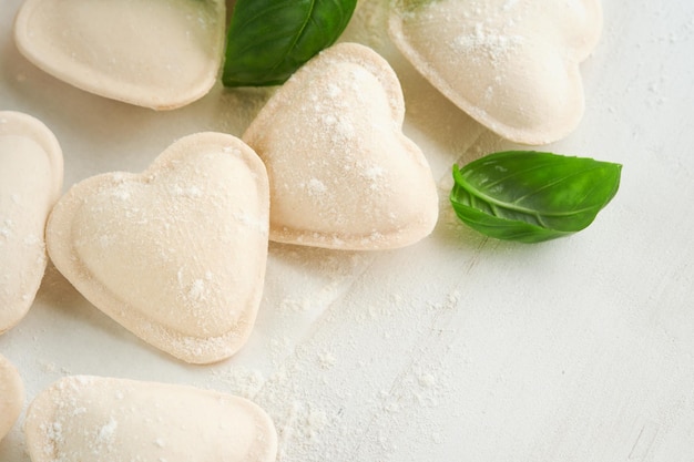Italian ravioli pasta in heart shape Tasty raw ravioli with flour and basil on white background Food cooking ingredients background Valentines or Mothers Day lunch ideas Top view with copy space
