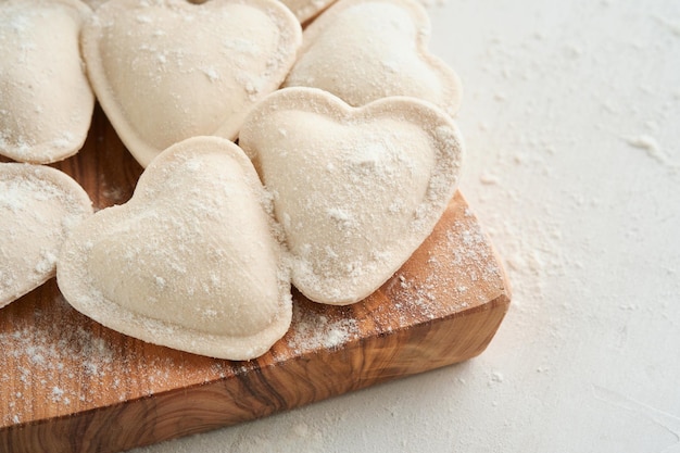 Italian ravioli pasta in heart shape Tasty raw ravioli with flour and basil on white background Food cooking ingredients background Valentines or Mothers Day lunch ideas Top view with copy space