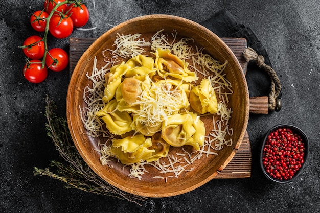 Italian ravioli Pasta with Mozzarella cheese and Tomato in wooden plate. Black background. Top view.