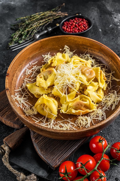 Italian ravioli Pasta with Mozzarella cheese and Tomato in wooden plate. Black background. Top view.