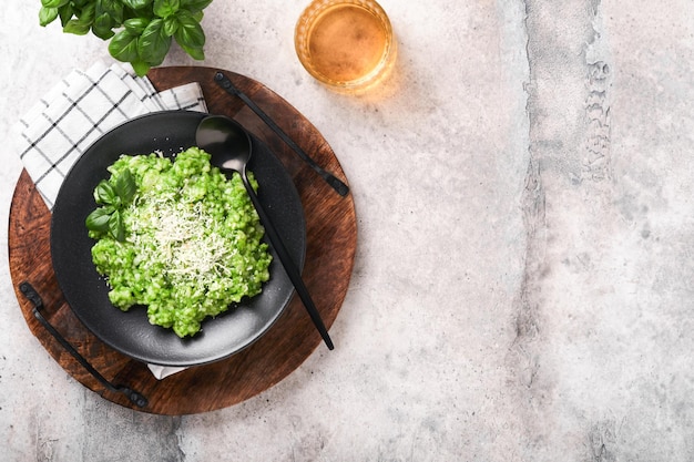 Italian risotto Delicious risotto in white plate with pesto sauce or wild garlic pesto basil parmesan cheese and glass of white wine on old light grey table background Top view with copy space