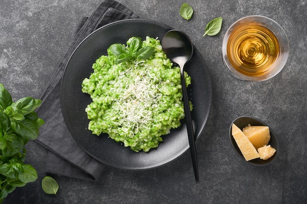 Italian risotto delicious risotto with pesto sauce or wild\
garlic pesto basil parmesan cheese and glass of white wine on dark\
slate table background italian dinner top view with copy space