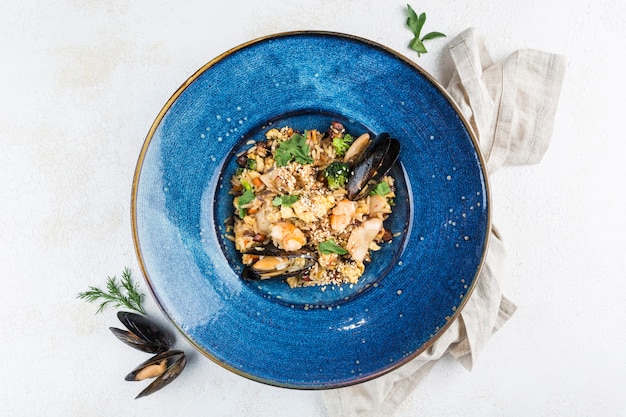 Italian risotto with mussels on a blue plate with a napkin on a light background. Top view with a copy space for the text. Food from the restaurant. Horizontal orientation.