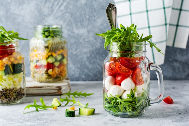 Italian salad of arugula, mozzarella and cherry tomato served in a jar for lunch on the table. Selective focus.