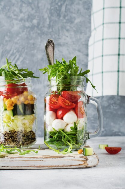 Italian salad of arugula, mozzarella and cherry tomato served in a jar for lunch on the table. Selective focus.