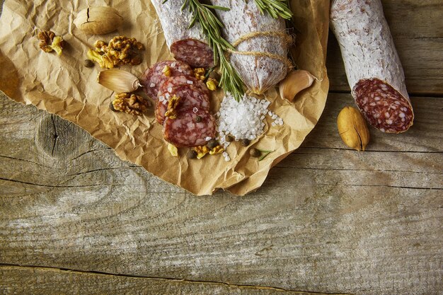 Foto salame italiano con sale marino, rosmarino, aglio e noci su carta stile rustico primo piano