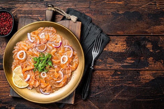 Italian Salmon carpaccio with onion and arugula served on a plate Wooden background Top view Copy space