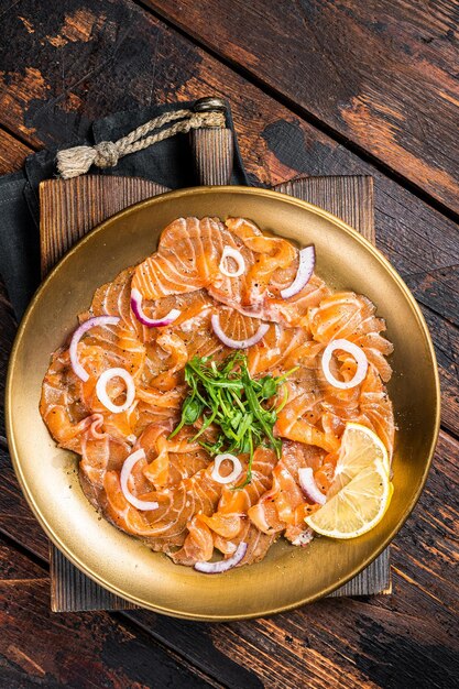 Foto carpaccio di salmone italiano con cipolla e rucola servito su un piatto fondo in legno vista dall'alto