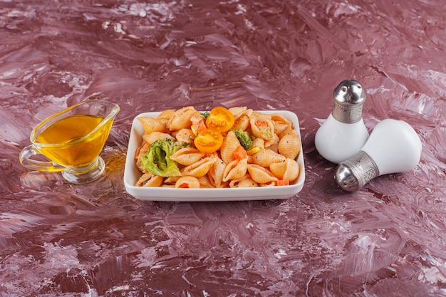 Italian shell pasta with oil and mixed vegetables on light table .