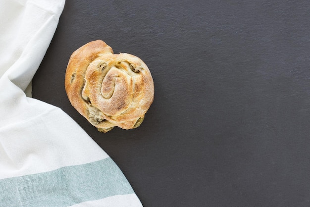 Italian snail bread roll with olives on black background