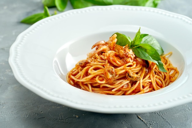 Italian spaghetti pasta with tomatoes and shrimps in a white plate on a gray background