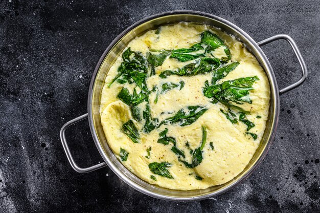 Italian Spinach and Cheese Omelet in a pan.  Black background.