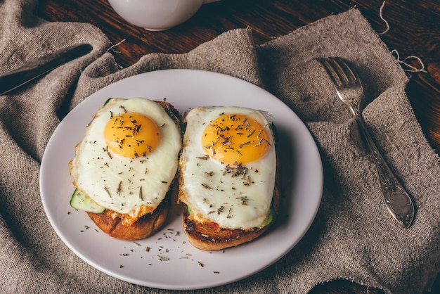 Italian toasts with vegetables and fried eggs on white plate and cup of coffee over grey rough cloth.