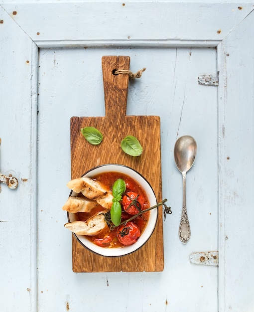 イタリアのトマト、ニンニク、バジルのスープパパアルポモドーロ、金属製のボウルにパンと素朴な木の板に水色のテーブルの上