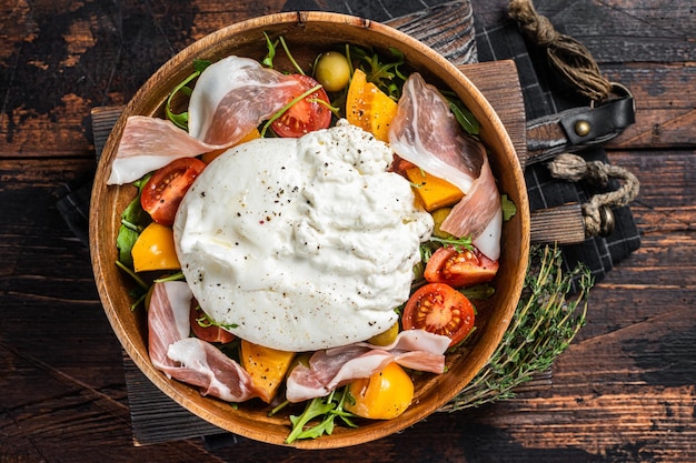 Insalata di pomodori italiani e burrata con prosciutto crudo di rucola e olive sfondo in legno vista dall'alto