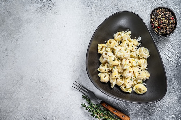 Italian tortellini pasta in cream sauce
with spinach. White wooden background. Top view. Copy space.