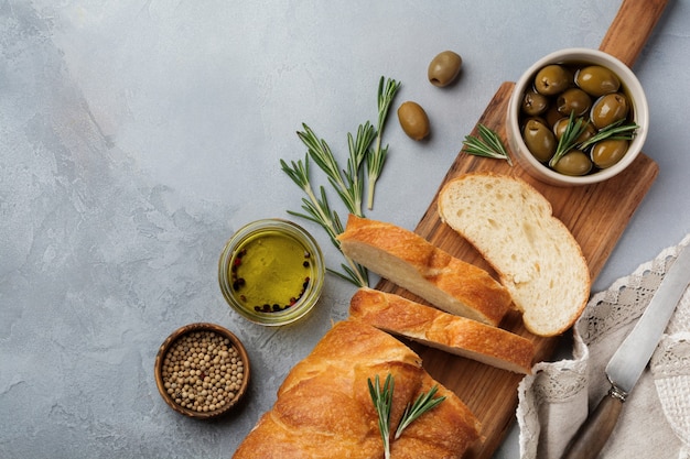 Italian traditional Ciabatta bread with olives, olive oil, pepper and rosemary on light gray concrete surface