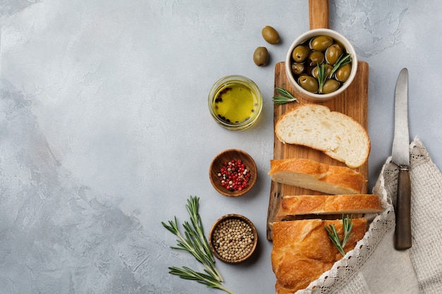 Итальянский традиционный хлеб чиабатта с оливками, оливковым маслом, перцем и розмарином на светло-сером каменном или бетонном фоне. Выборочный фокус. Вид сверху. Скопируйте пространство.
