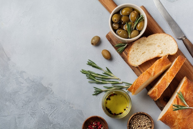 Pane ciabatta tradizionale italiano con olive, olio d'oliva, pepe e rosmarino su pietra grigio chiaro o superficie in cemento