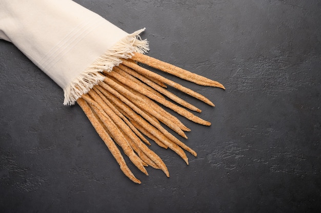 Italian traditional rye bread grissini on linen napkin on dark background.