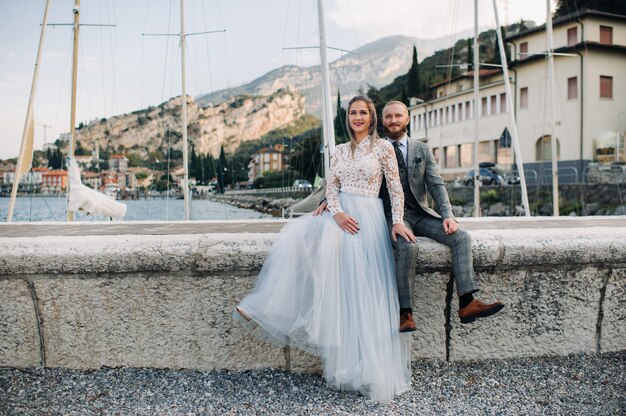 Italië, Gardameer. Een mooi stel aan de oevers van het Gardameer in Italië aan de voet van de Alpen. Een man en een vrouw zitten op een pier in Italië.