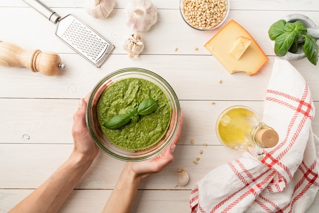 Cucina italiana. preparazione del pesto italiano fatto in casa. pesto fresco in una ciotola con ingredienti, vista dall'alto piatta su un tavolo di legno bianco, spazio copia