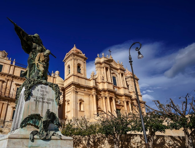 Photo italy, sicily, noto (siracusa province), view of the s. nicolò cathedral baroque facade (1703) and the world war 1 momument