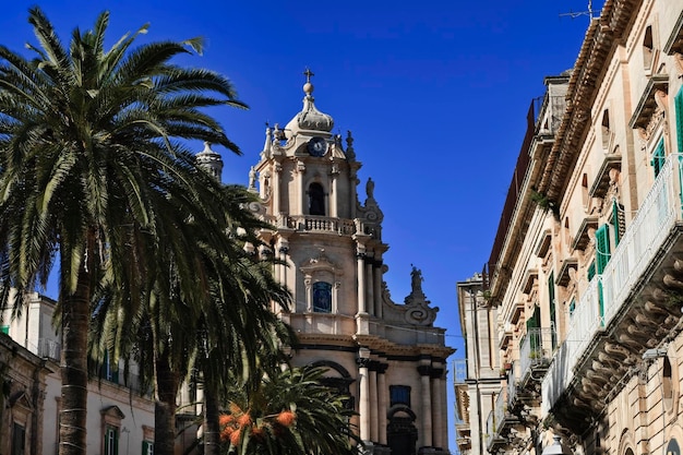 Foto italia. sicilia, ragusa ibla, palme, vecchi edifici barocchi e la facciata barocca della cattedrale di san giorgio